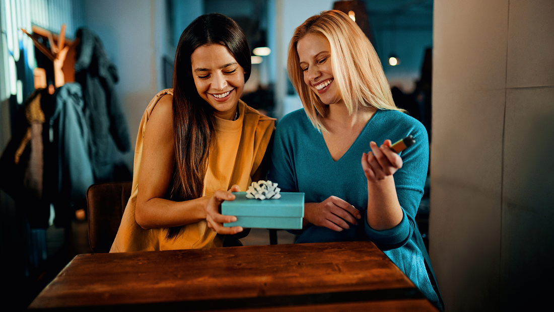 Două femei care se uită la o cutie de cadou și zâmbesc