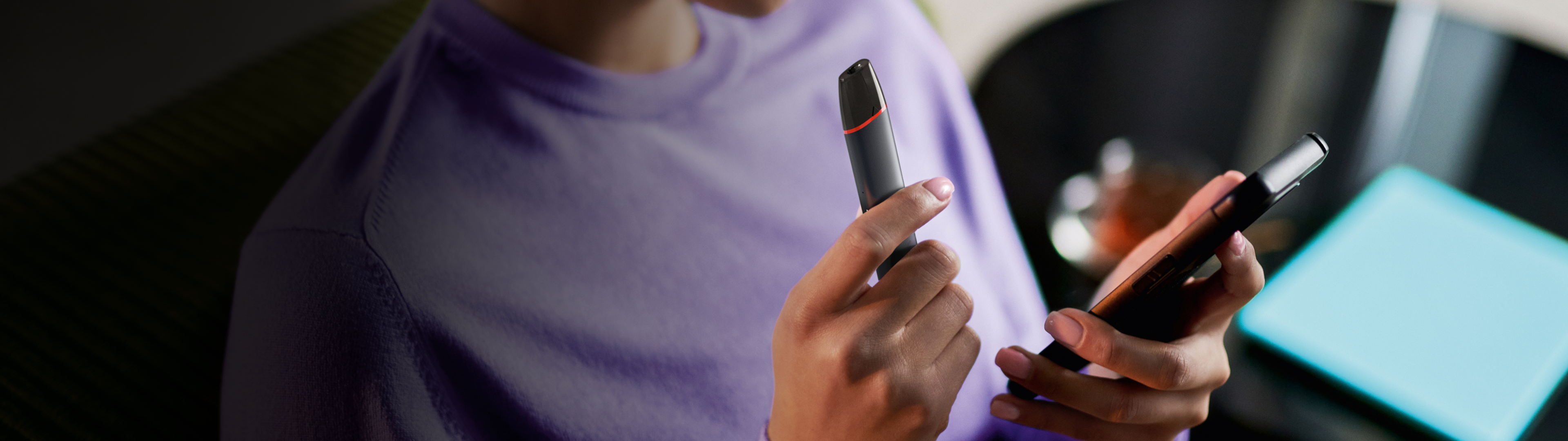 Mâini care țin un dispozitiv de vapat VEEV inPRIME negru și un telefon