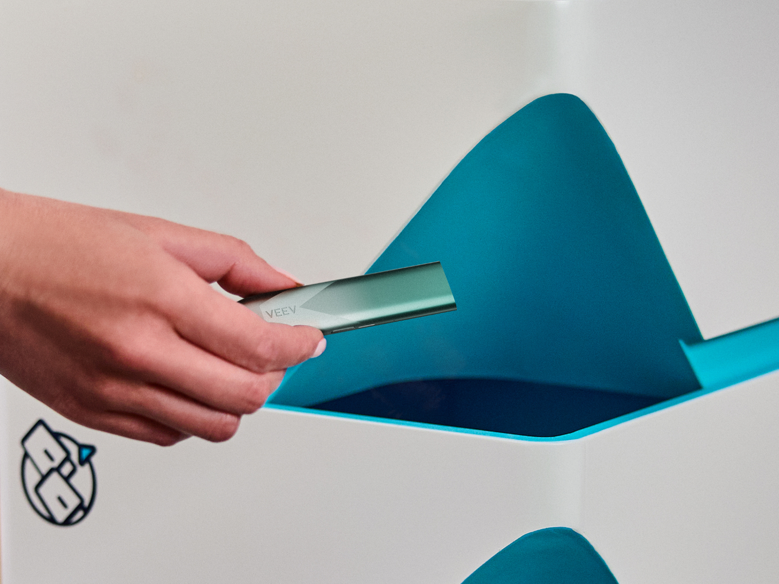 Imagine - Mână care ține un dispozitiv de vapat VEEV inPRIME verde - punct de reciclare VEEV în fundal