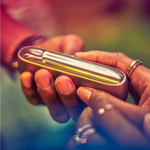 O persoană care ține un dispozitiv IQOS Gold