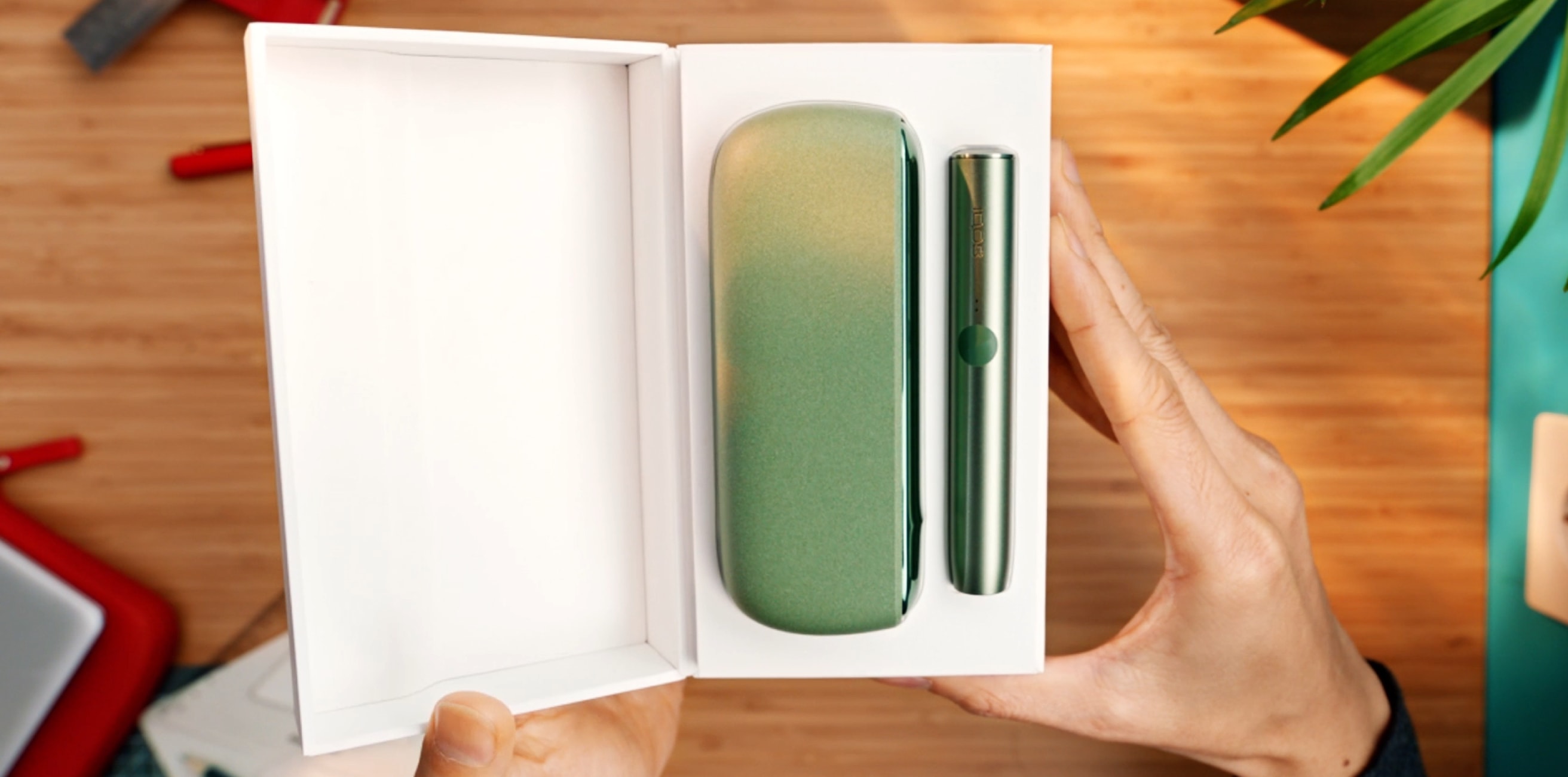 Un stilou IQOS ILUMA și un încărcător portabil în culoarea Moss Green